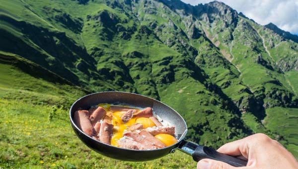Сковородка с яичницей и сосисками на фоне природы