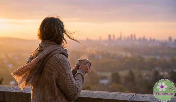 Девушка с чашкой кофе смотрит на город с балкона